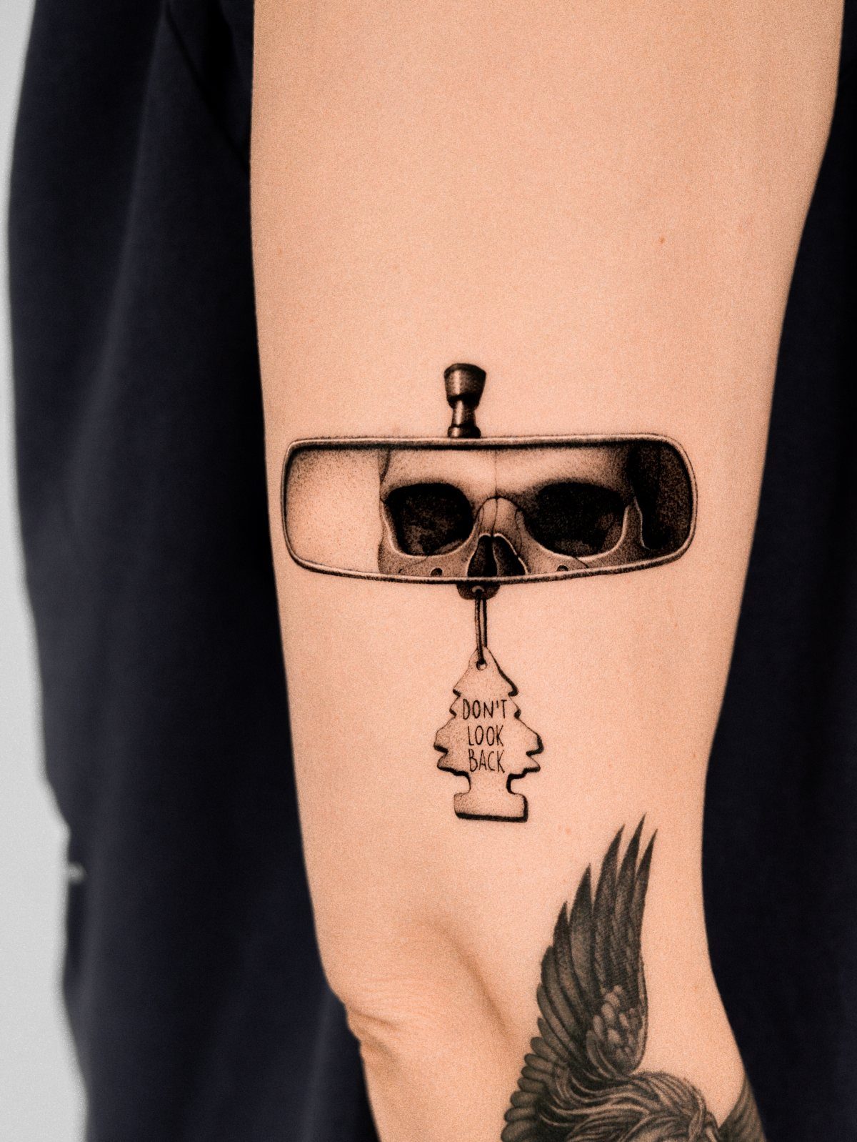 Tattoo of a rearview mirror reflecting a skull with a Don't Look Back tag.