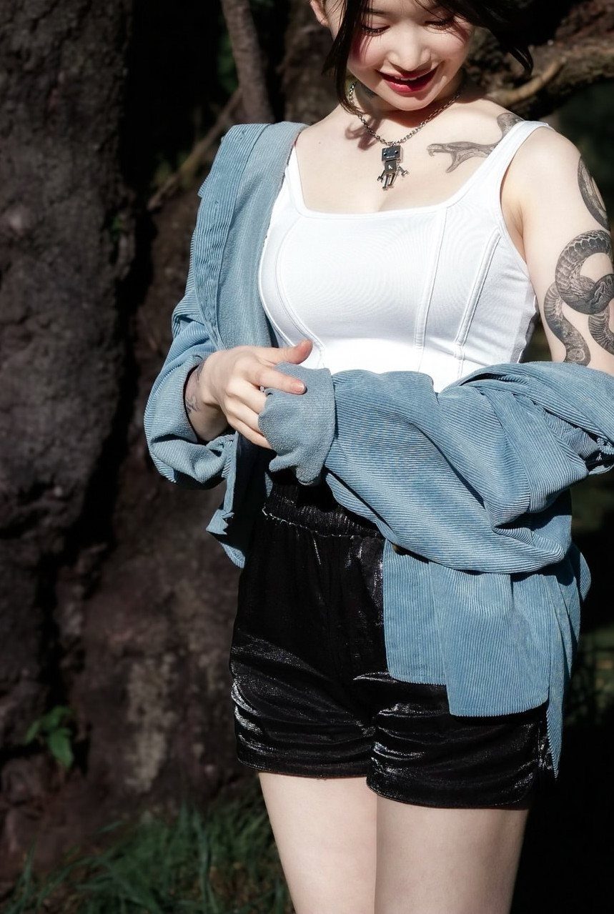 Woman with a large snake tattoo on her arm posing by a tree.
