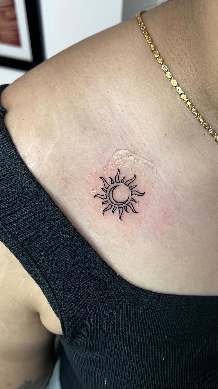 Sun and moon tattoo on a person's collarbone with a protective clear bandage.