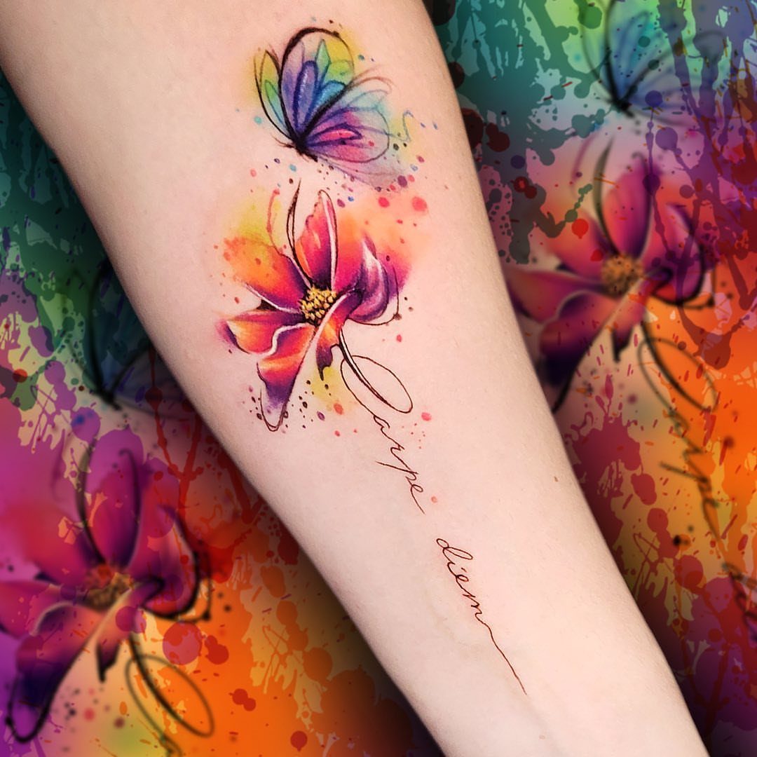Watercolor tattoo on a forearm featuring a butterfly, a flower, and cursive text.