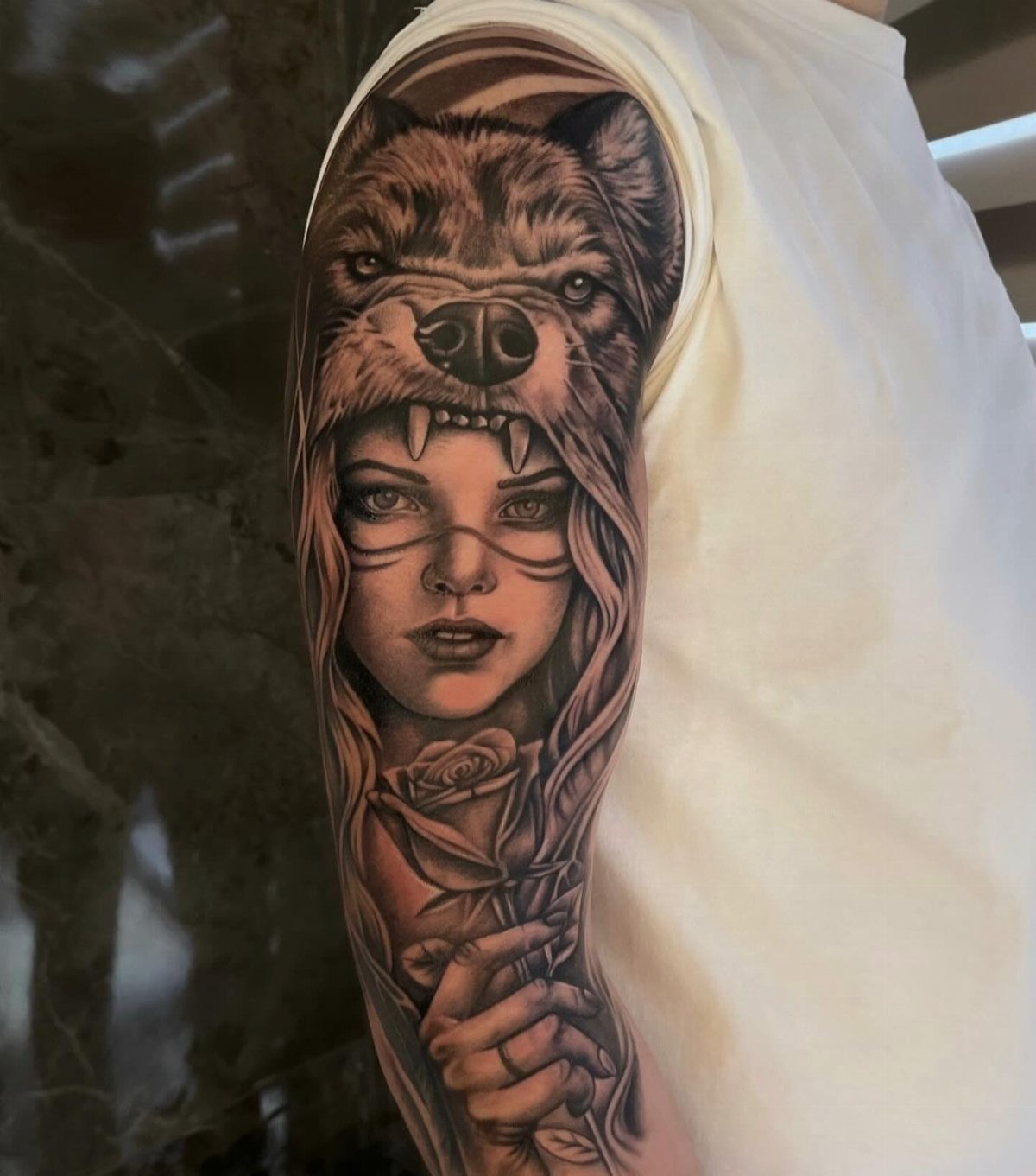 Woman's arm tattoo featuring a female face wearing a wolf pelt and holding a rose.