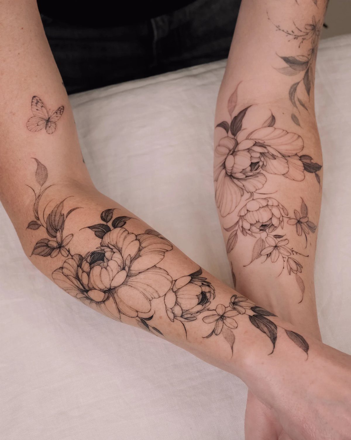 Minimalist Fine Line Tattoo Ideas: 9 Styles to Consider 1 Fine line flower tattoos of peonies and leaves on two forearms.