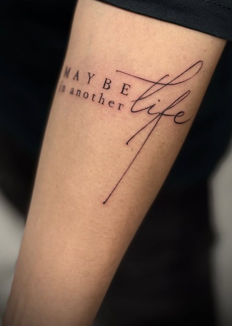 Minimalist Fine Line Tattoo Ideas: 9 Styles to Consider 8 Fine line tattoo on a forearm reading MAYBE in another life in mixed fonts.