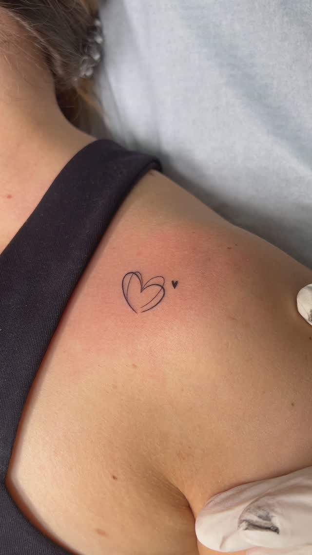 Minimalist Fine Line Tattoo Ideas: 9 Styles to Consider 6 Two small black fine line heart tattoos on a person's shoulder