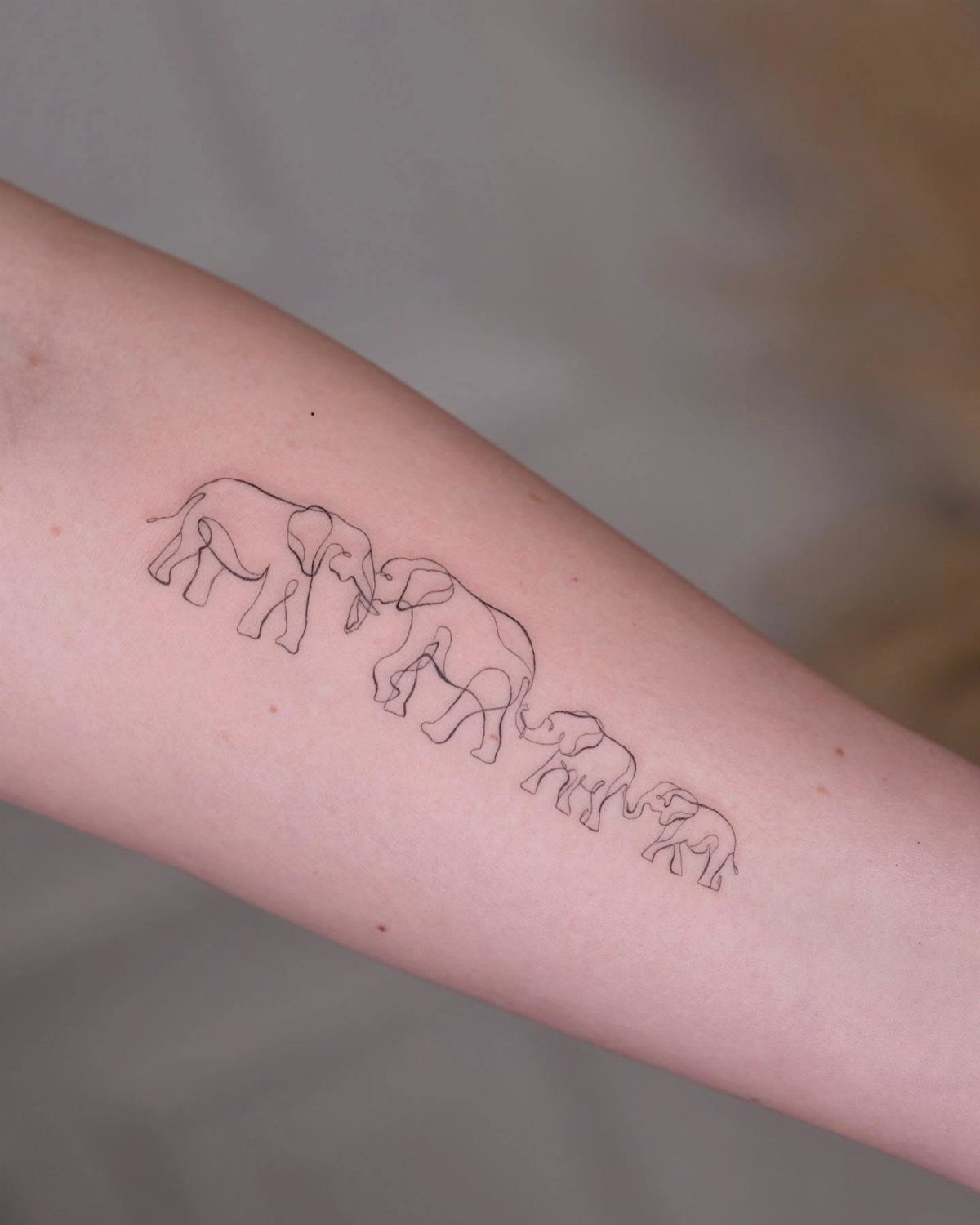 Line art tattoo of four elephants in a row on a forearm