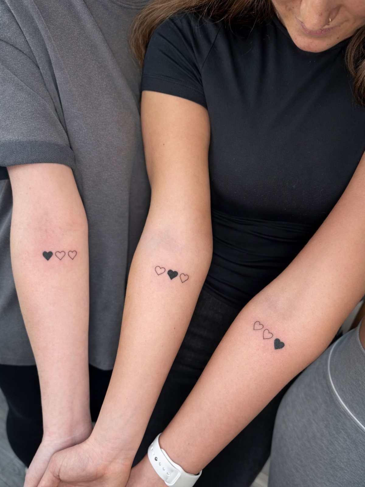 Three forearms with matching tattoos of three small hearts in a row.