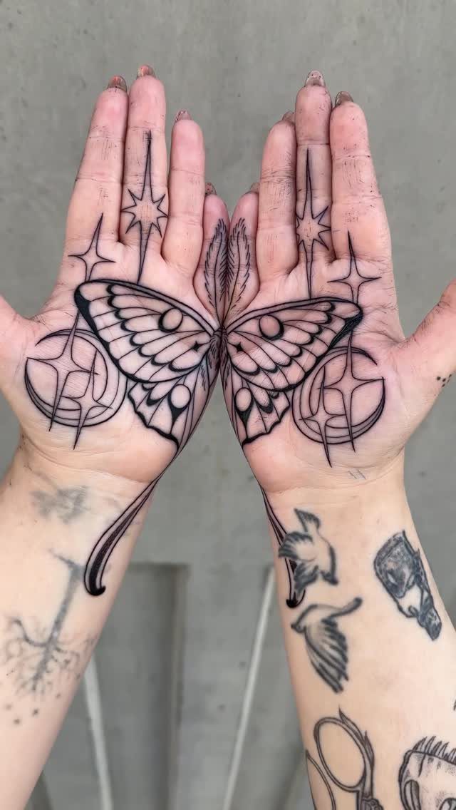 Symmetrical butterfly tattoo spanning across two open palms with accompanying star designs.