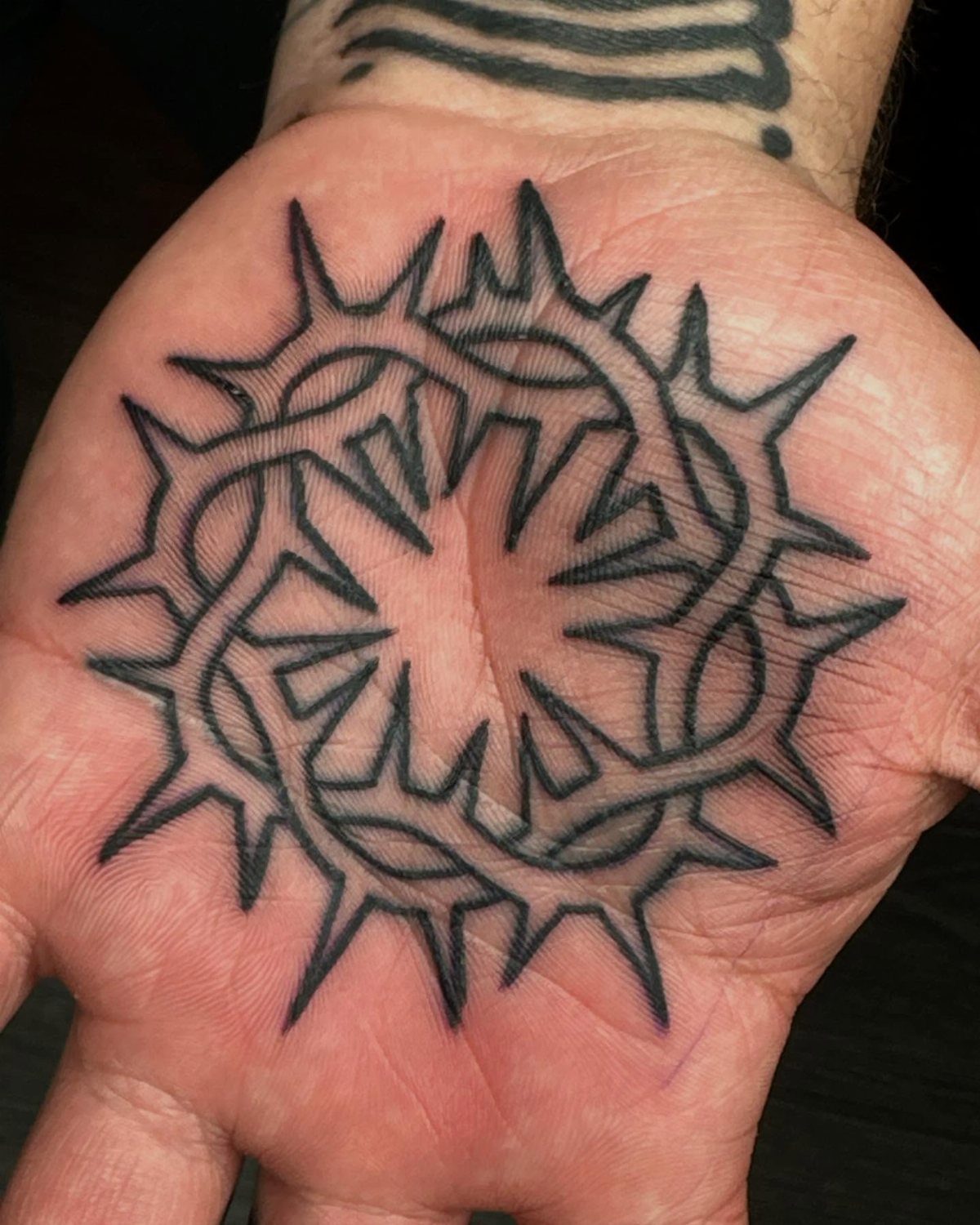 Circular thorny crown tattoo in black ink on the center of a palm.