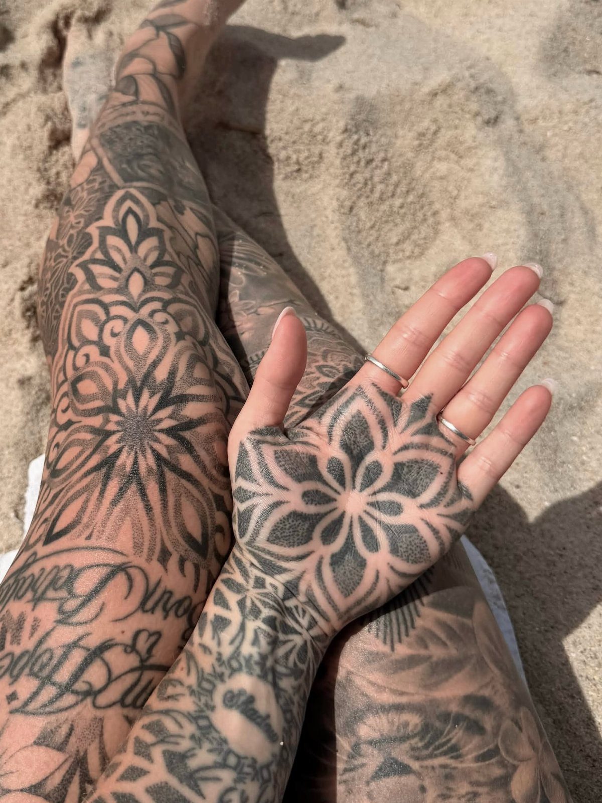 Geometric mandala tattoo on an open palm resting on sandy beach ground
