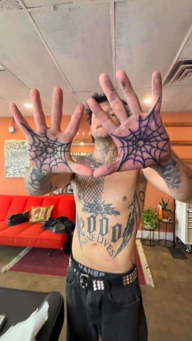 Man showing large black spider web tattoos on both of his open palms.