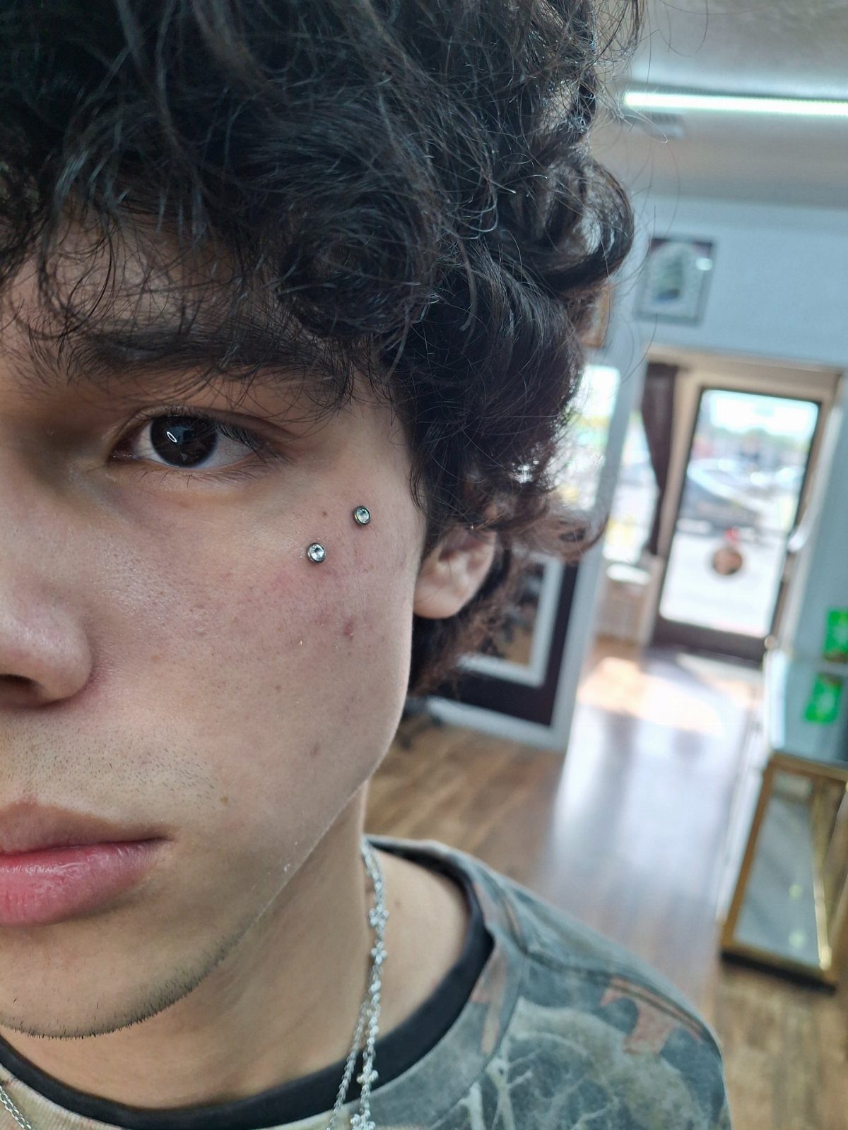 Piercing Between Eyebrows: 8 Styles and Placements 2 Young man with curly hair showing two silver stud piercings on his cheekbone.