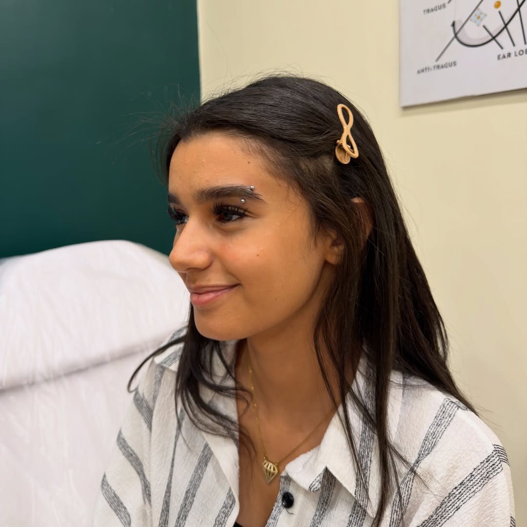 Piercing Between Eyebrows: 8 Styles and Placements 6 Young woman smiling with a small metal stud piercing between her eyebrows.