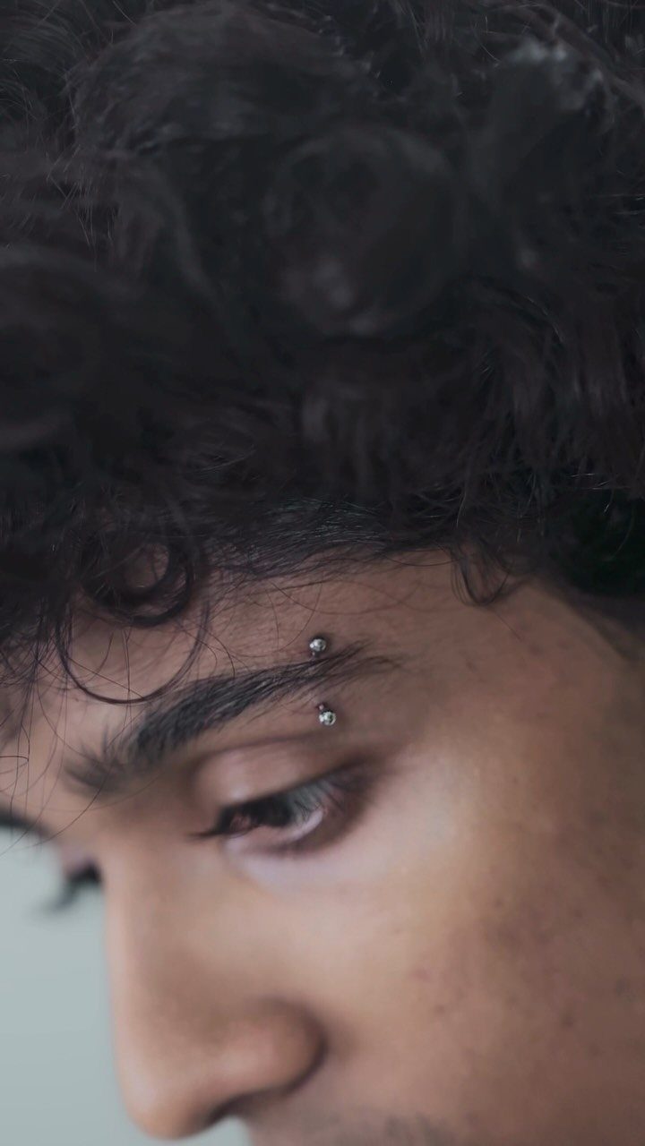 Piercing Between Eyebrows: 8 Styles and Placements 5 Person's forehead and eyebrow area featuring two silver stud bridge piercings.