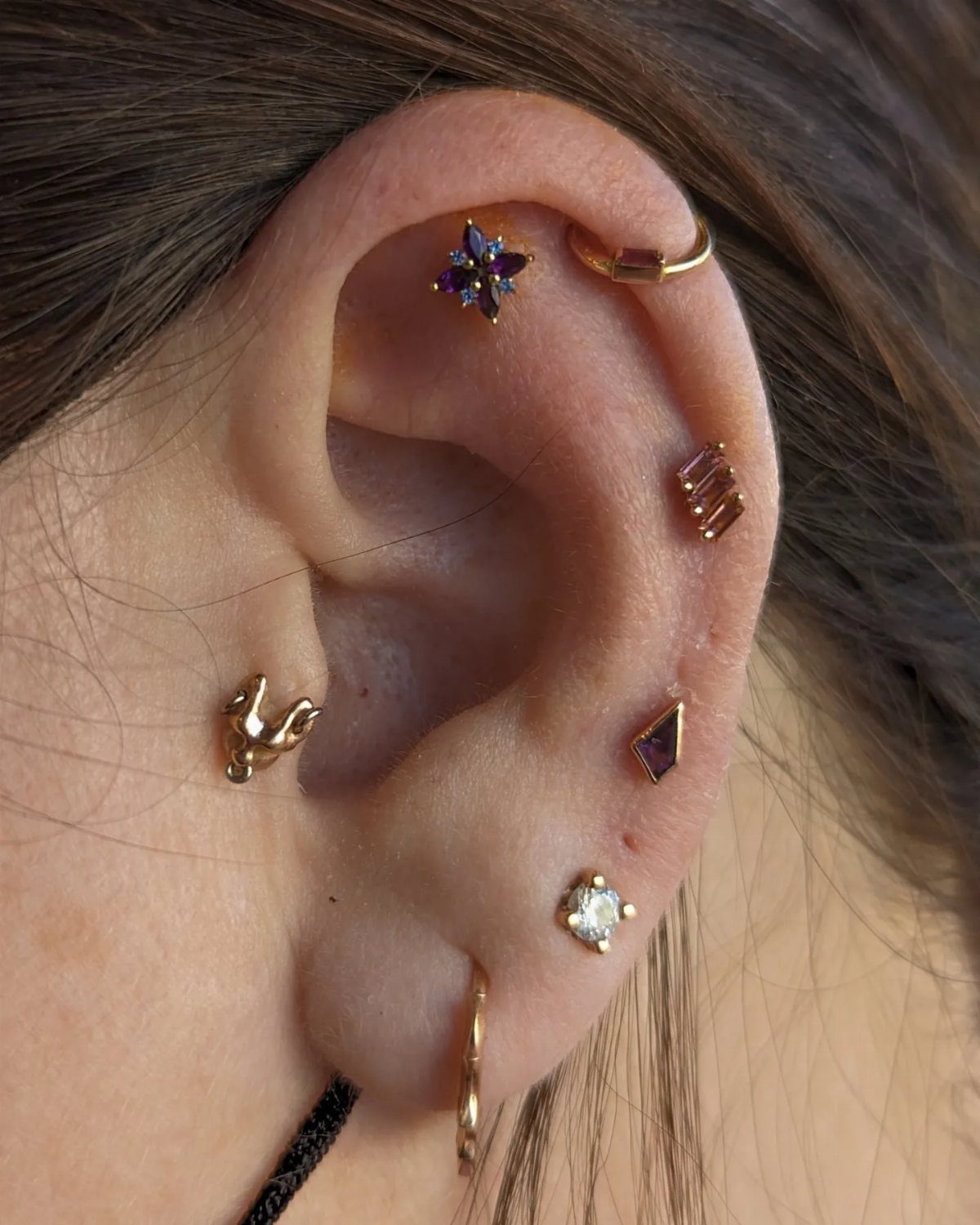 Human ear with multiple gold piercings, featuring a star stud on the flat area.