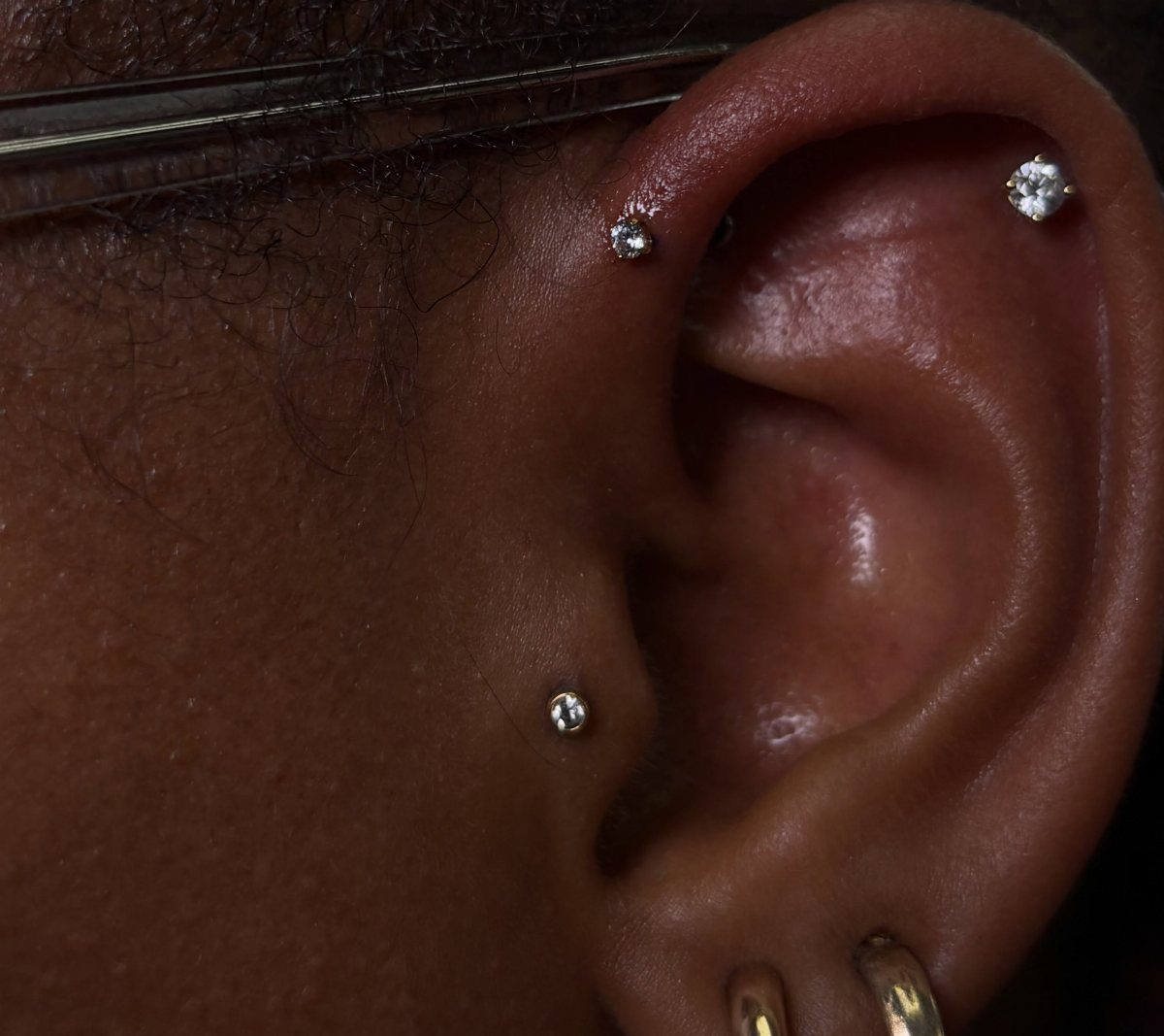 Ear with gemstone studs in the forward helix and tragus and gold lobe hoops