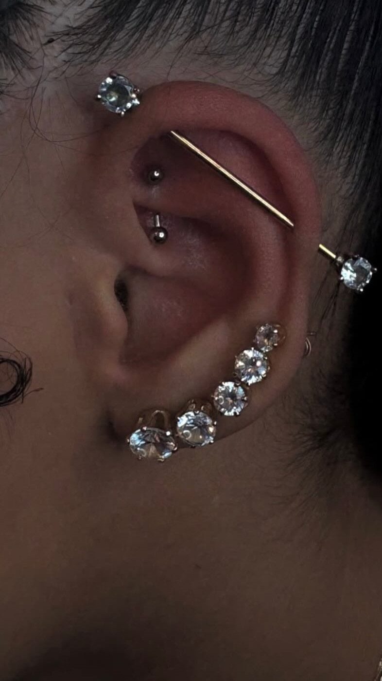 Ear with a gold industrial barbell piercing and multiple diamond studs on the lobe.