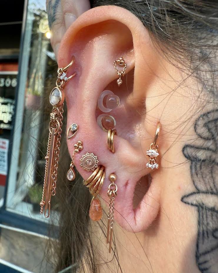 Human ear with multiple gold piercings, stretched lobes, and various gemstone jewelry.
