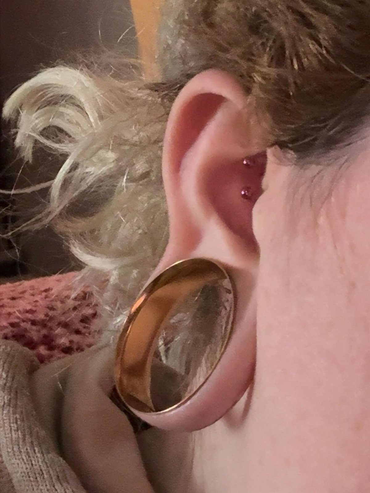 Stretched earlobe with a large gold plug and small pink stud piercings.