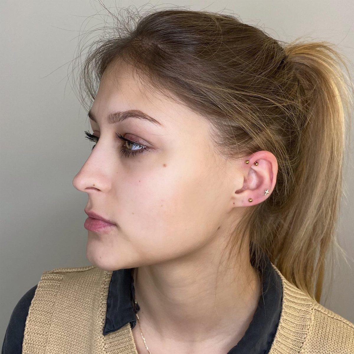 Woman with blonde hair showing multiple gold stud piercings in her ear lobe.