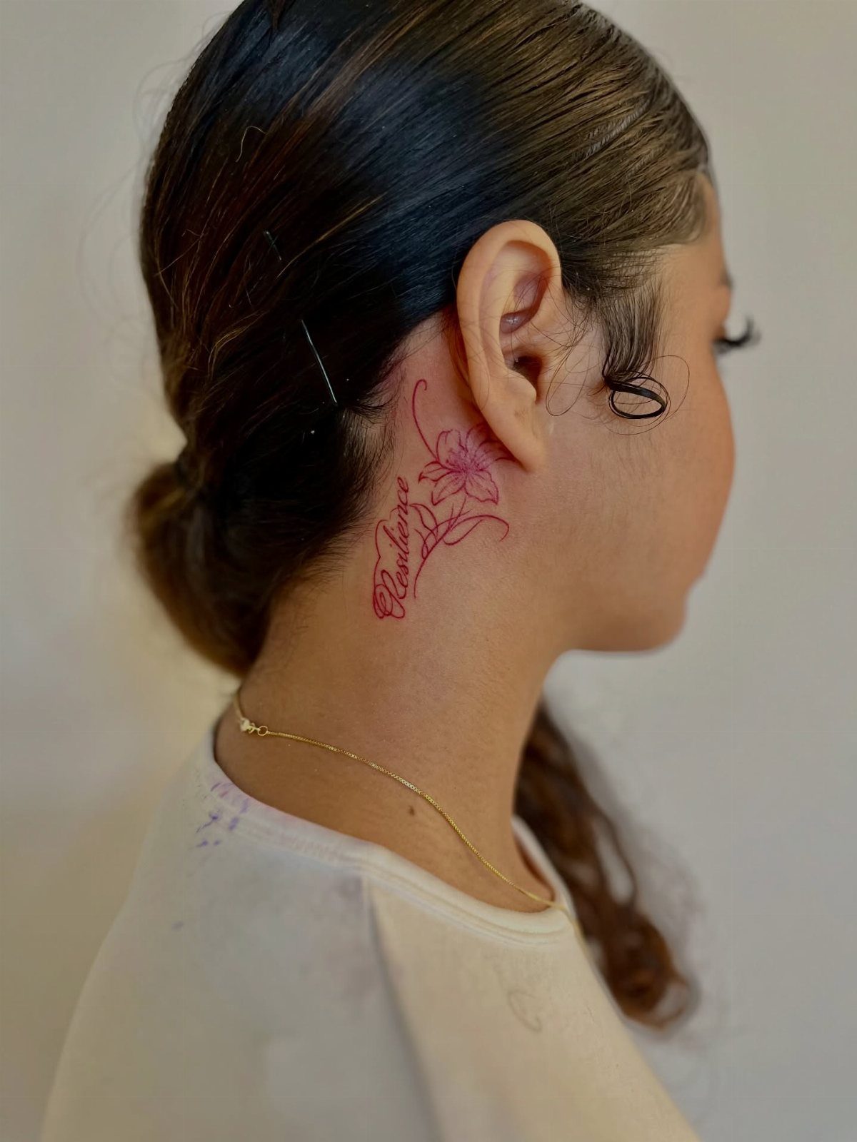 Woman with a red floral and script tattoo behind her right ear.