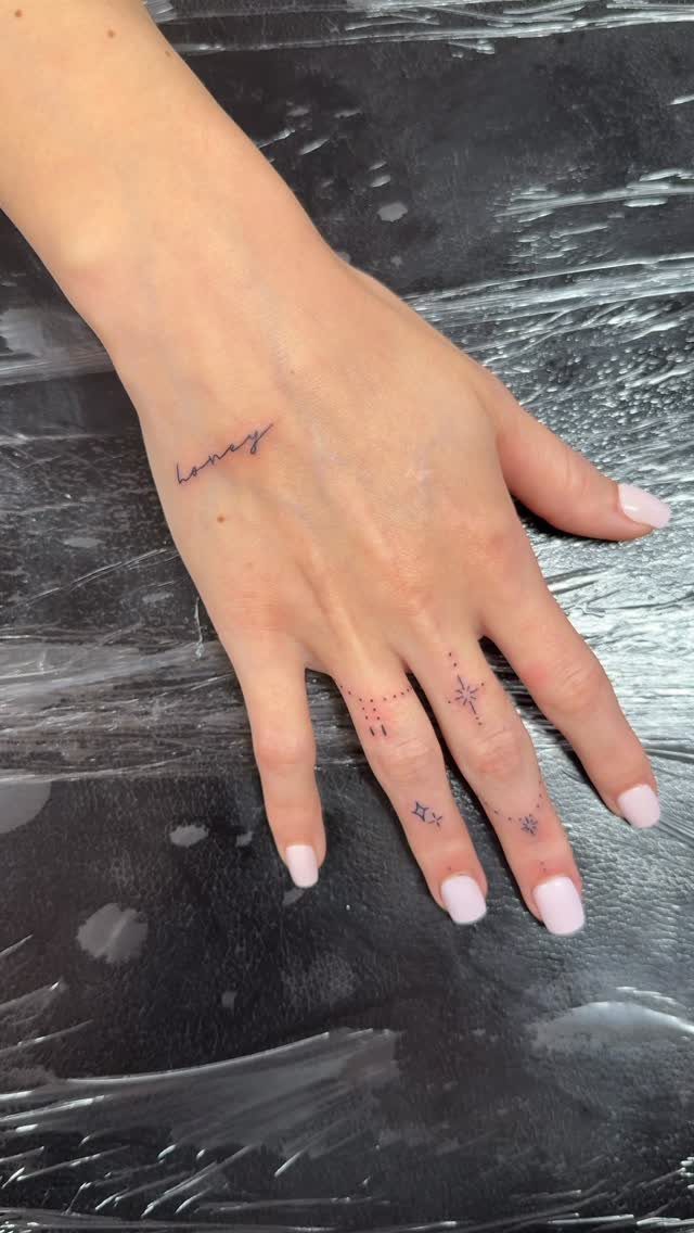 Woman's hand with small black ink tattoos on fingers and side of hand.