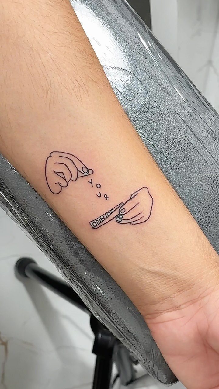 Inner forearm tattoo of two hands holding a slip of paper saying your opinion