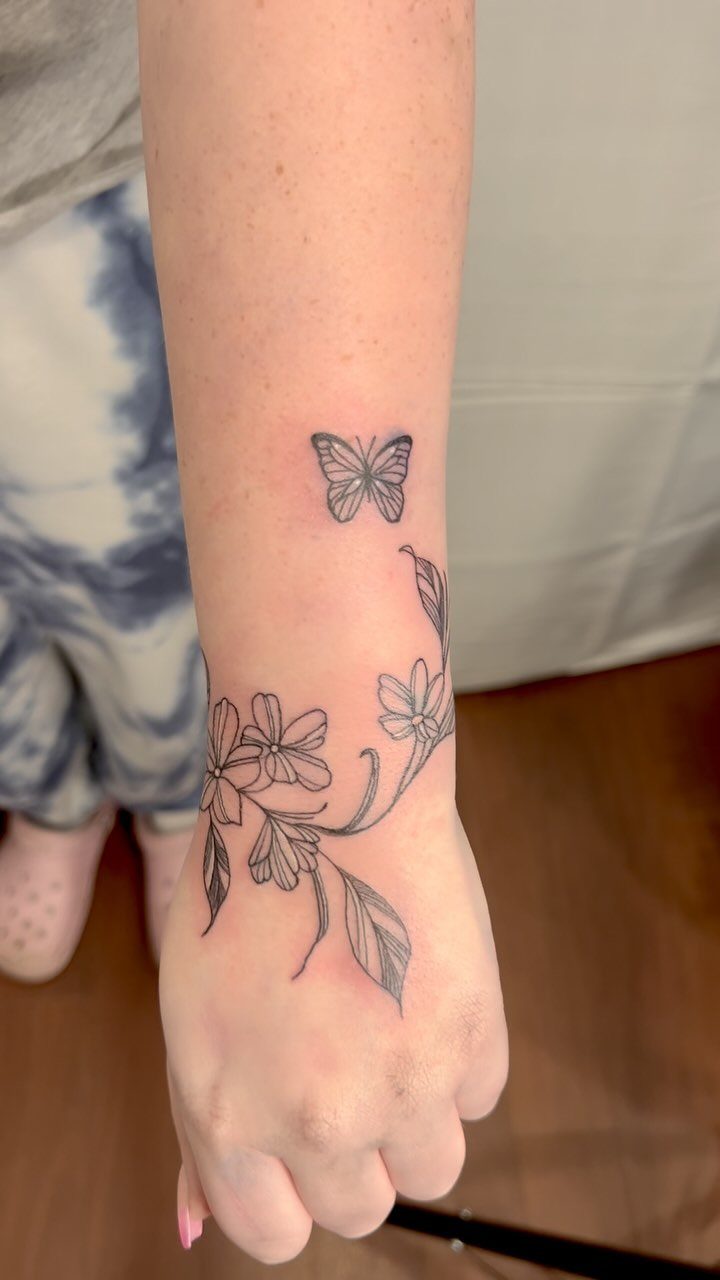 Inner wrist tattoo featuring a small butterfly and delicate floral vine designs.