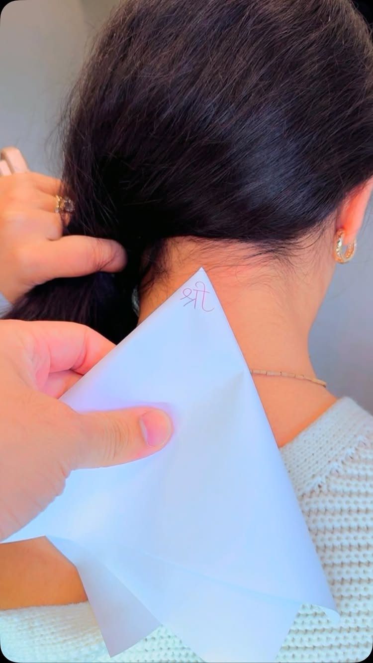 Small red script tattoo on the nape of a woman's neck with hair lifted.