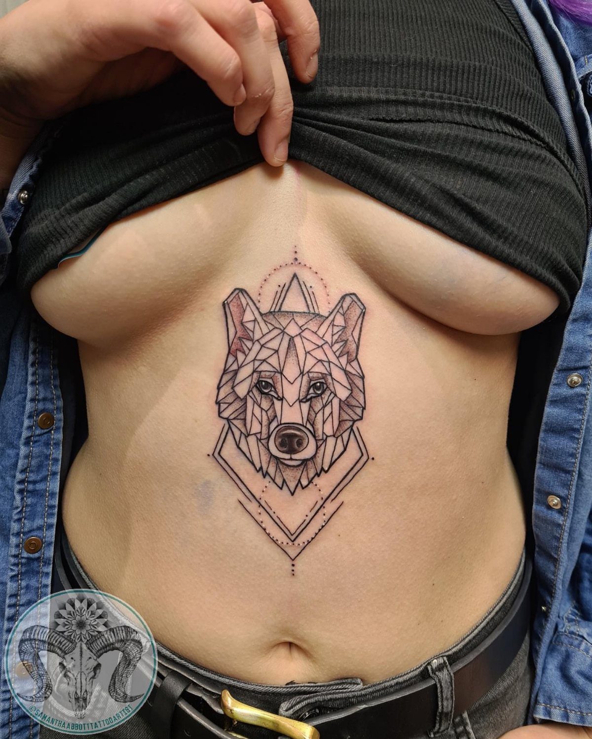 Geometric wolf head tattoo on a woman's sternum between the breasts
