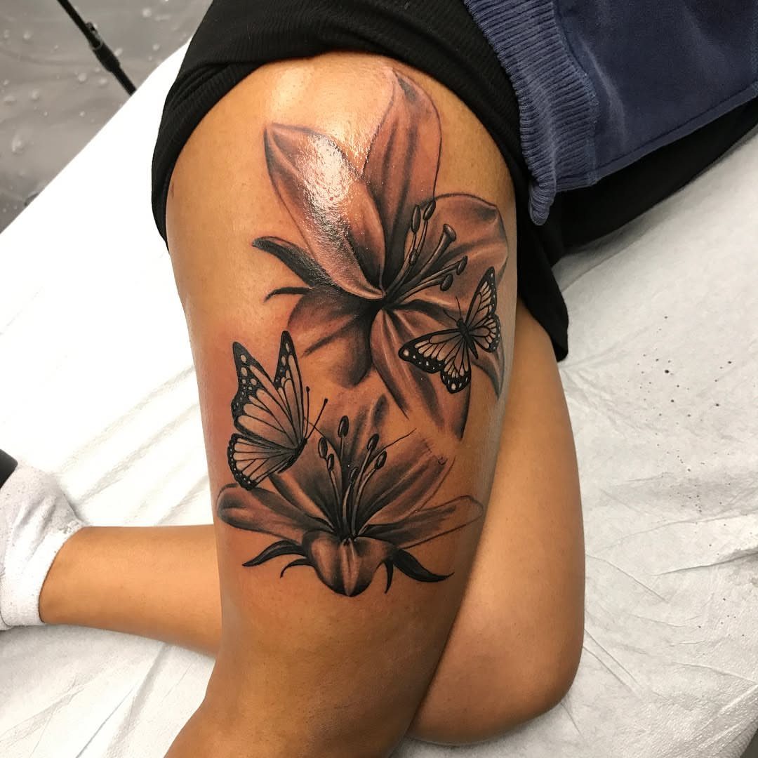 Thigh tattoo featuring detailed lilies and butterflies in black and grey ink.