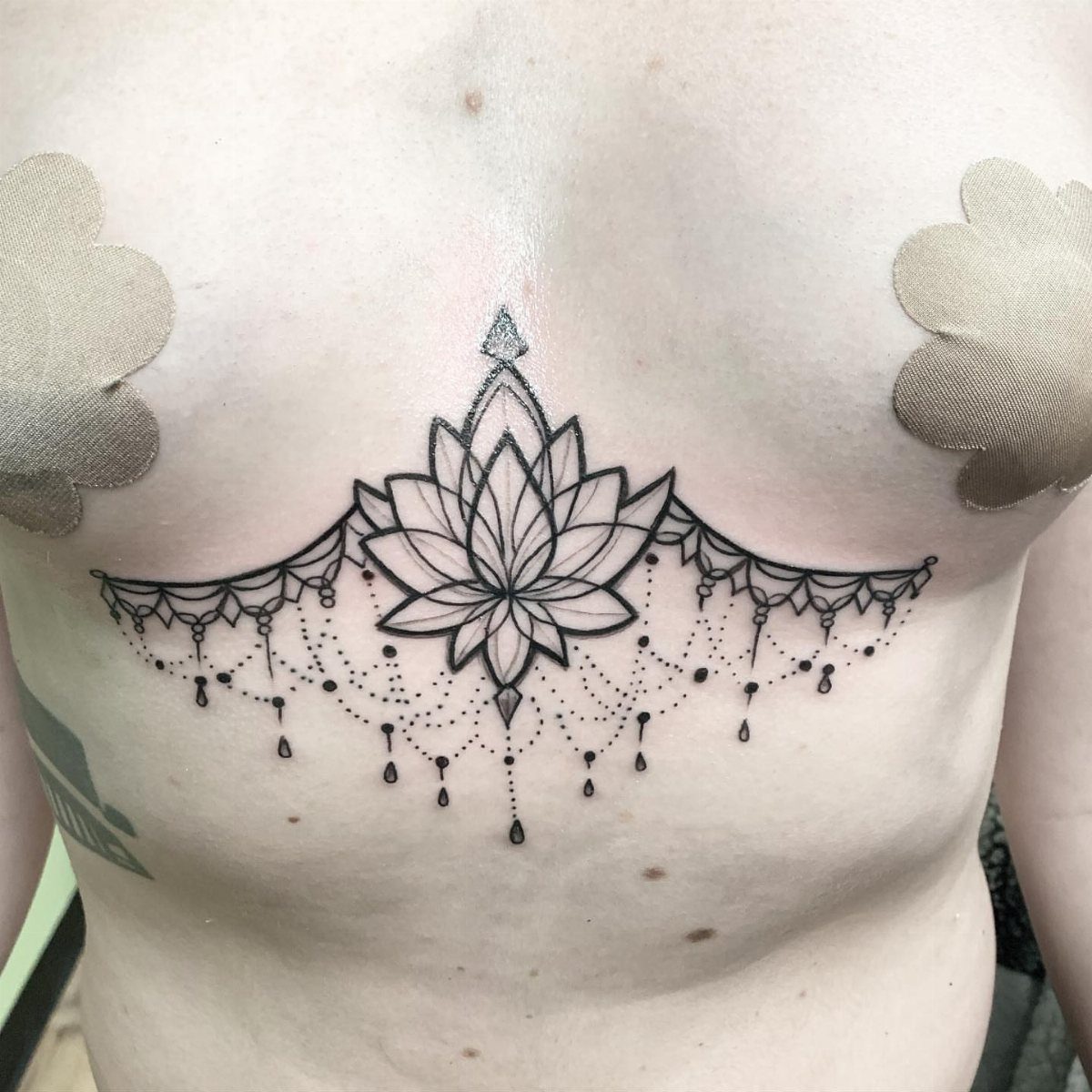 Lotus flower tattoo with beaded details located under the breasts on a woman