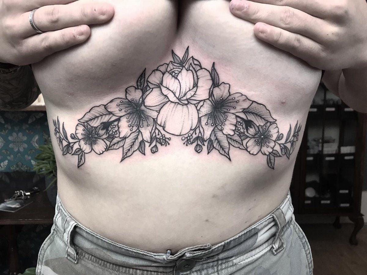 Floral tattoo on a person's abdomen featuring detailed black ink flowers and leaves.