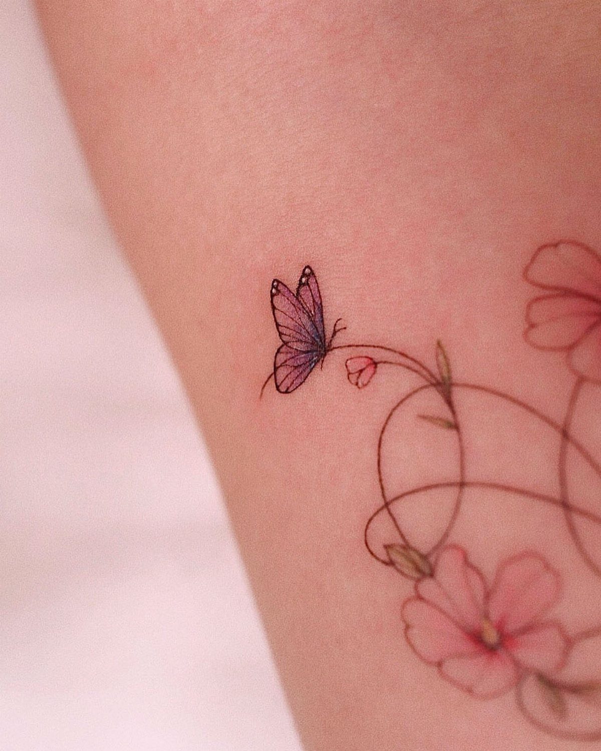Purple butterfly tattoo with pink flowers and swirling stems on fair skin.