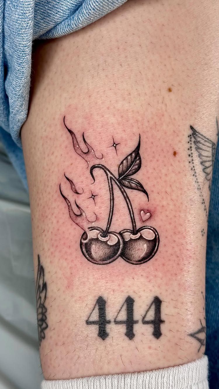 Cherry tattoo with flames and stars on a person's leg above the number 444