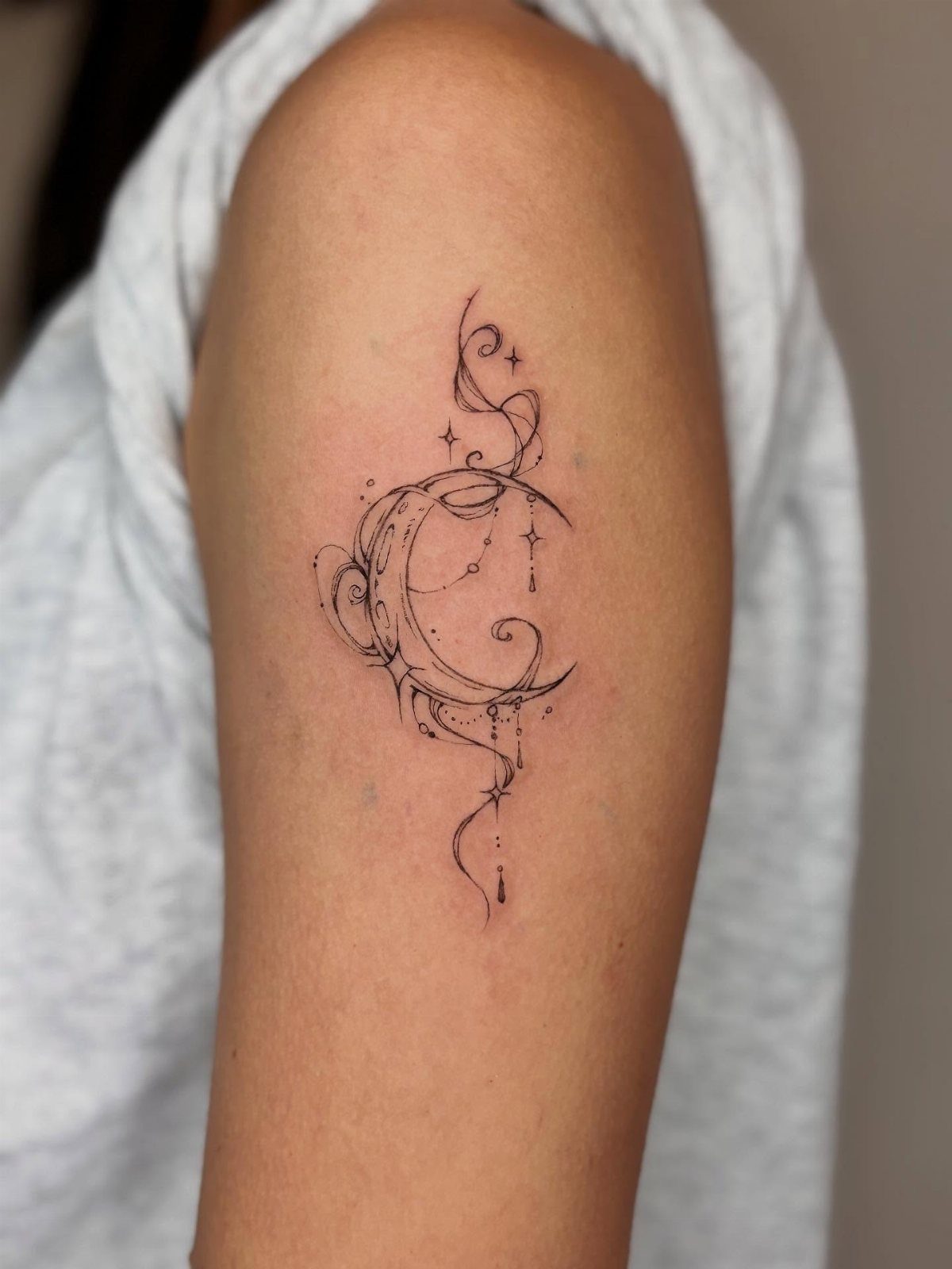 Crescent moon tattoo with stars and swirls on a person's upper arm.
