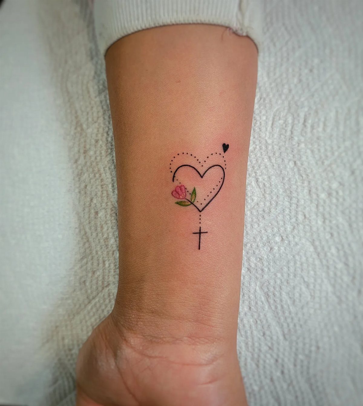 Heart tattoo on a wrist with a pink flower and a small cross.