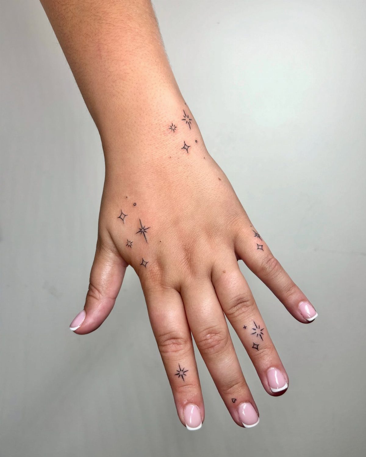 Hand and wrist with small black star tattoos and white French manicure nails.