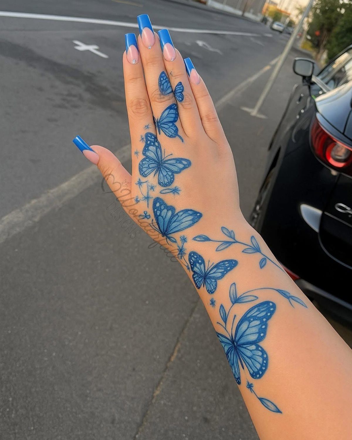 Hand and forearm with blue butterfly tattoos and long blue manicured nails.