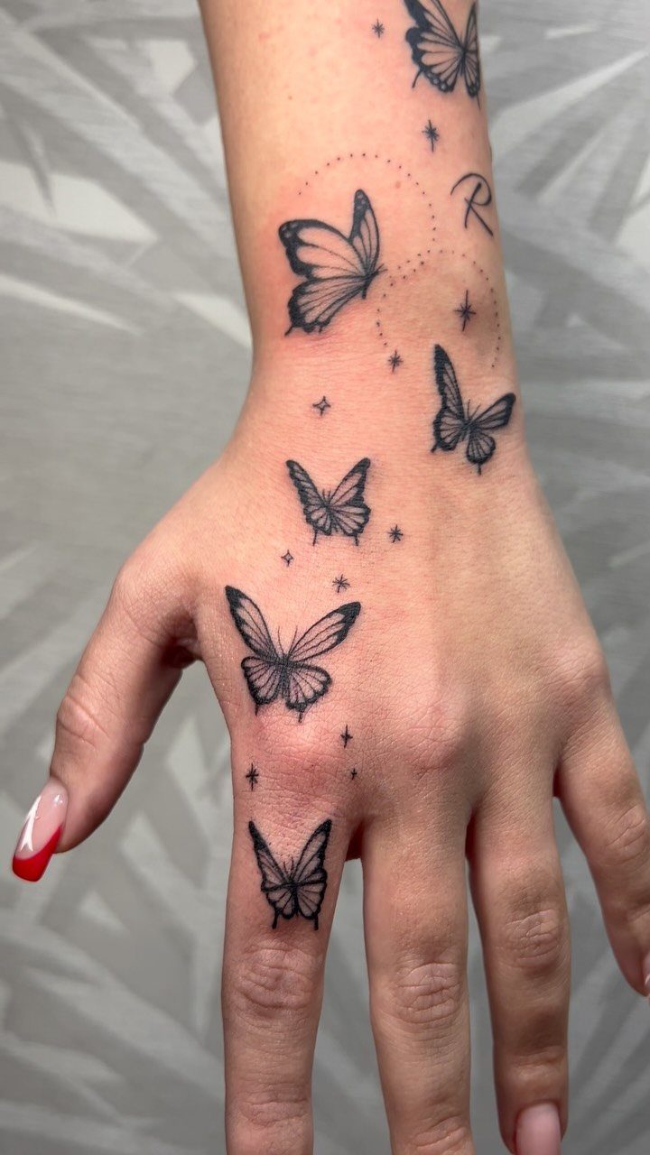 Hand and wrist with multiple black butterfly tattoos and small star accents.