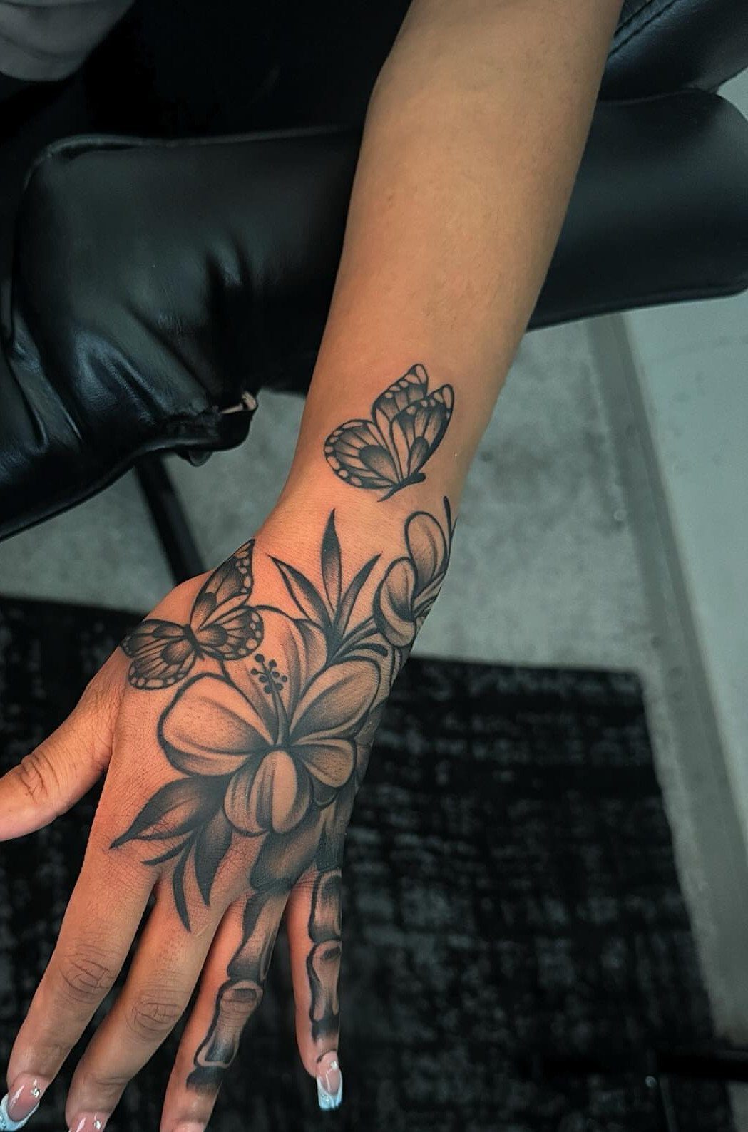 Hand and wrist with black ink tattoos of butterflies and floral patterns.