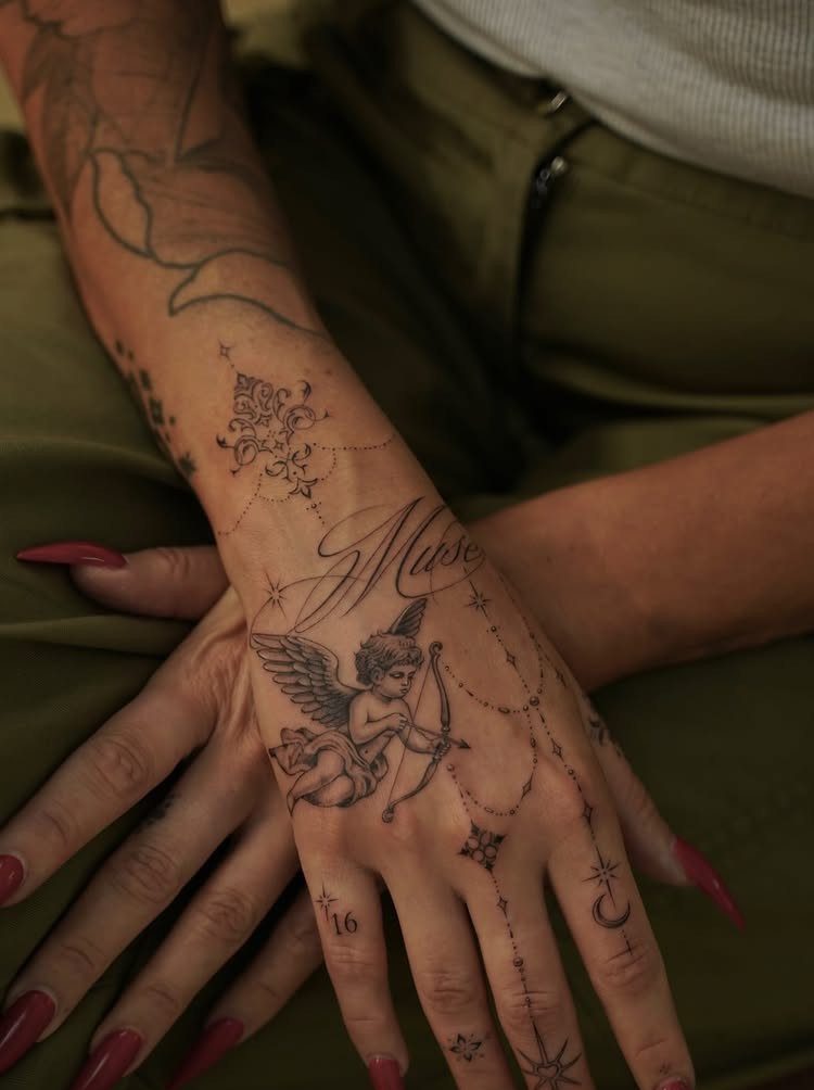 Hand with detailed black ink tattoos of a cherub and cursive text