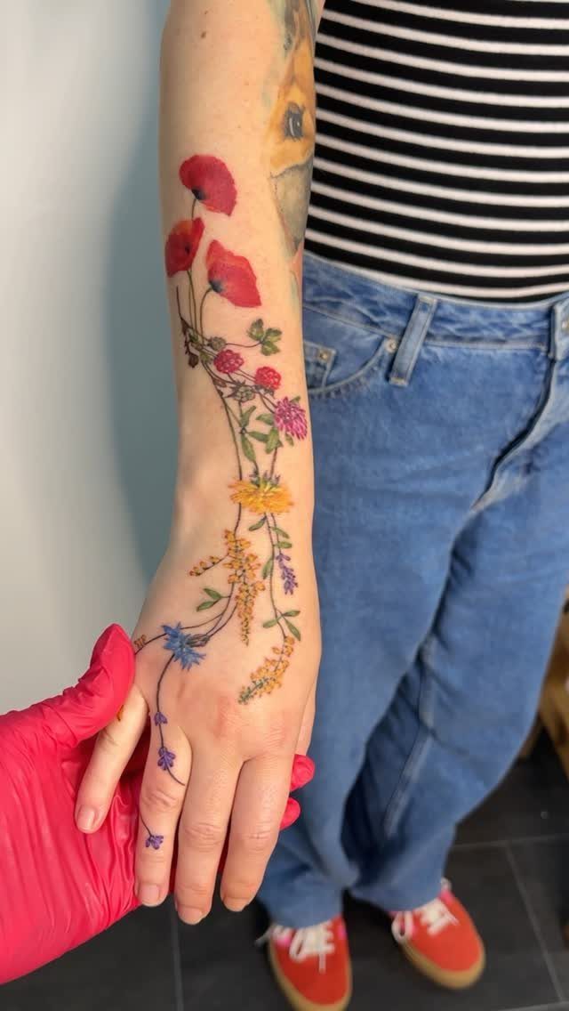 Colorful floral tattoo with red poppies and wildflowers on a person's hand and forearm.