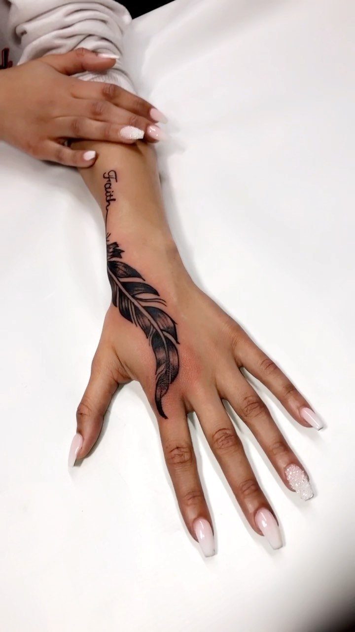 Hand and wrist with a black feather tattoo and the word Faith.