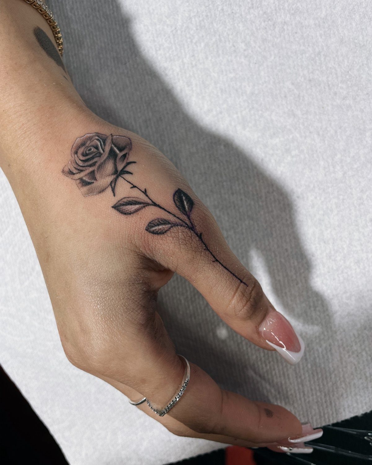 Rose sprig tattoo with thin lines on the back of a hand.
