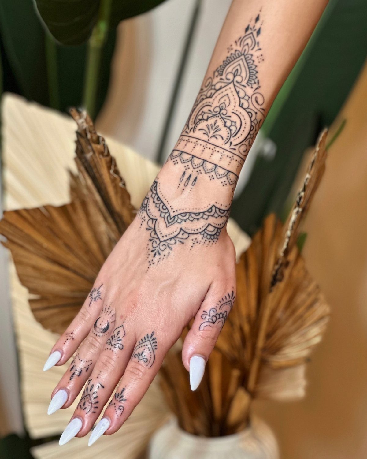 Hand and forearm with intricate black ink mandala tattoos and long white nails.