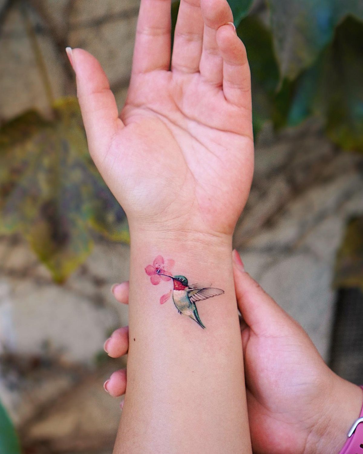 Small hummingbird tattoo sipping from a pink flower on a person's inner wrist.