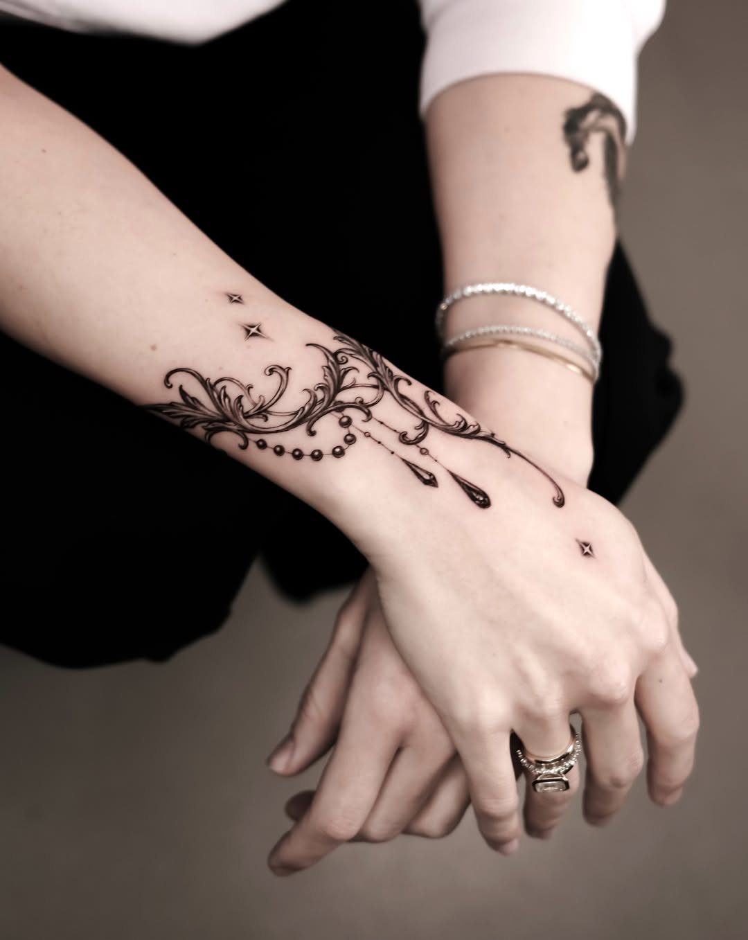 Ornamental black ink filigree tattoo on a person's wrist and hand.
