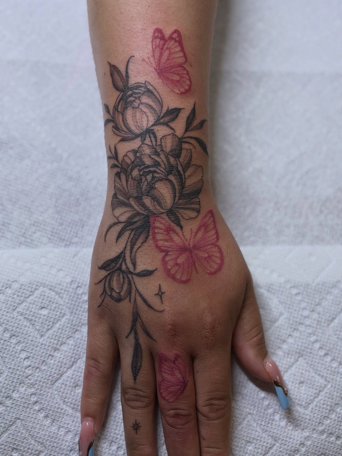 Hand and wrist with tattoos of black peonies and red butterflies on white background