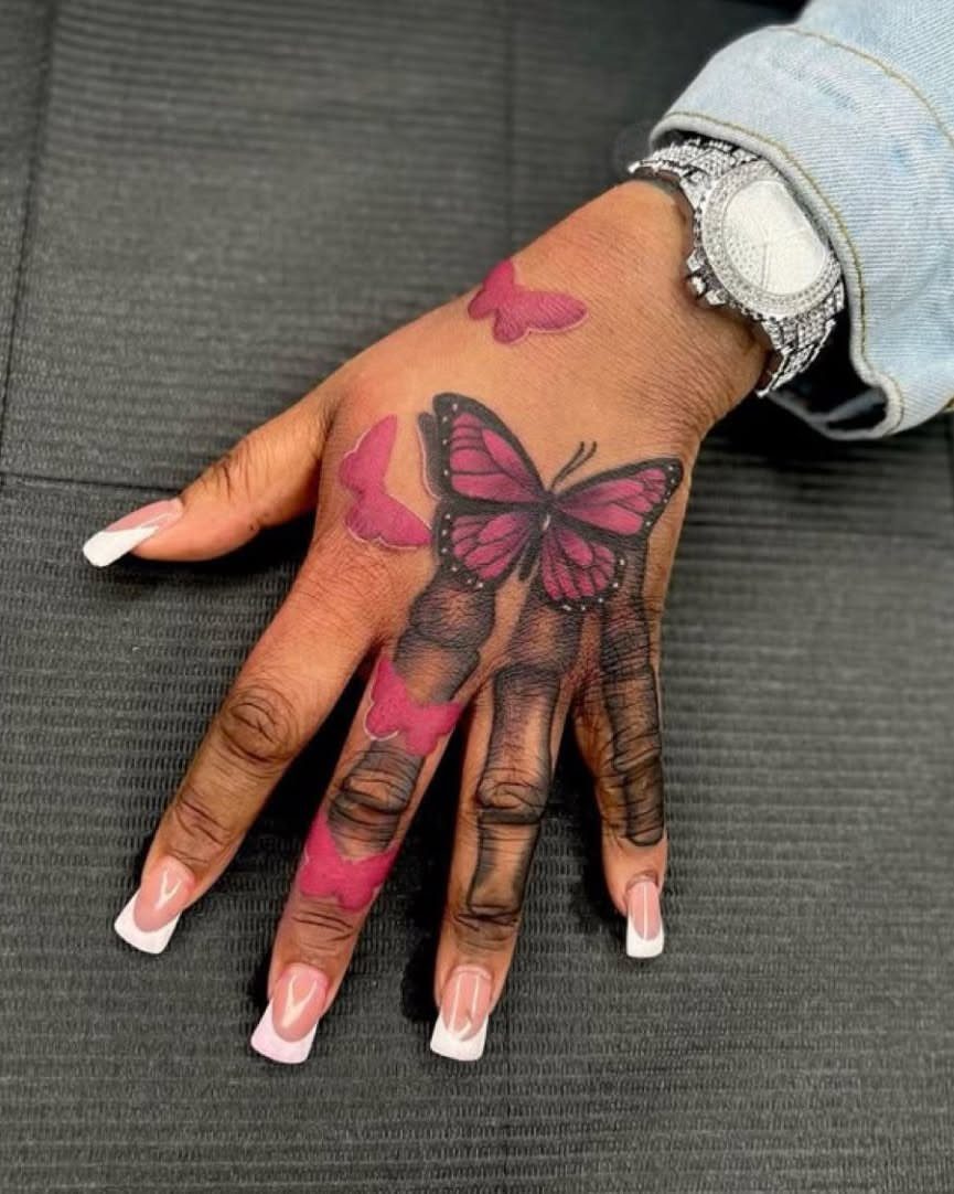 Hand with pink butterfly tattoos and long white-tipped nails wearing a silver watch