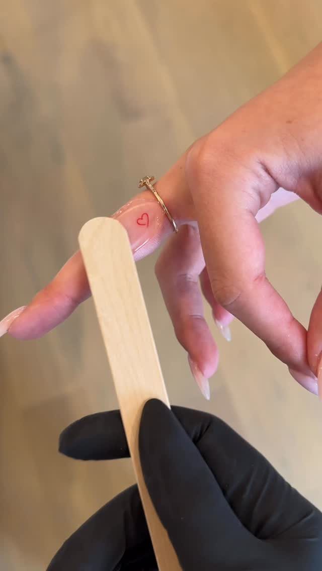 Small red heart tattoo on the side of a finger with a silver ring.